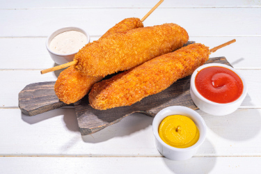 Mexican corn dogs on a wooden board next to condiments