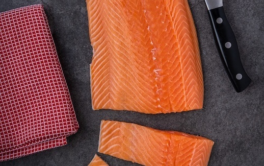 salmon on cutting board near a knife and kitchen towel